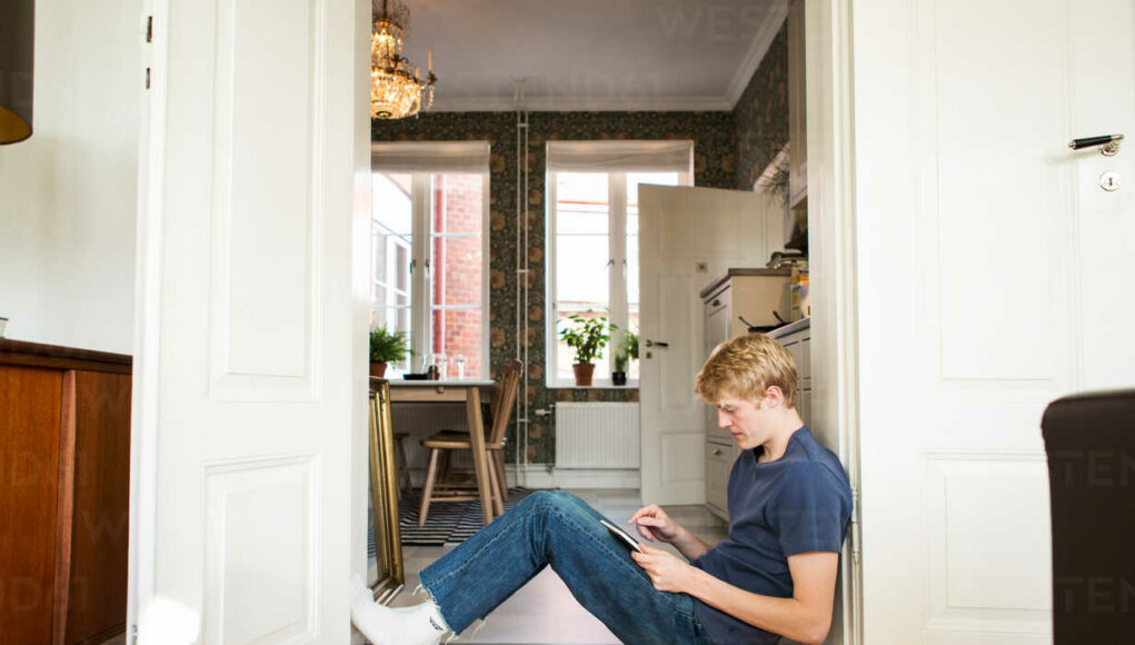 Side view of young man using digital tablet while sitting at doorway